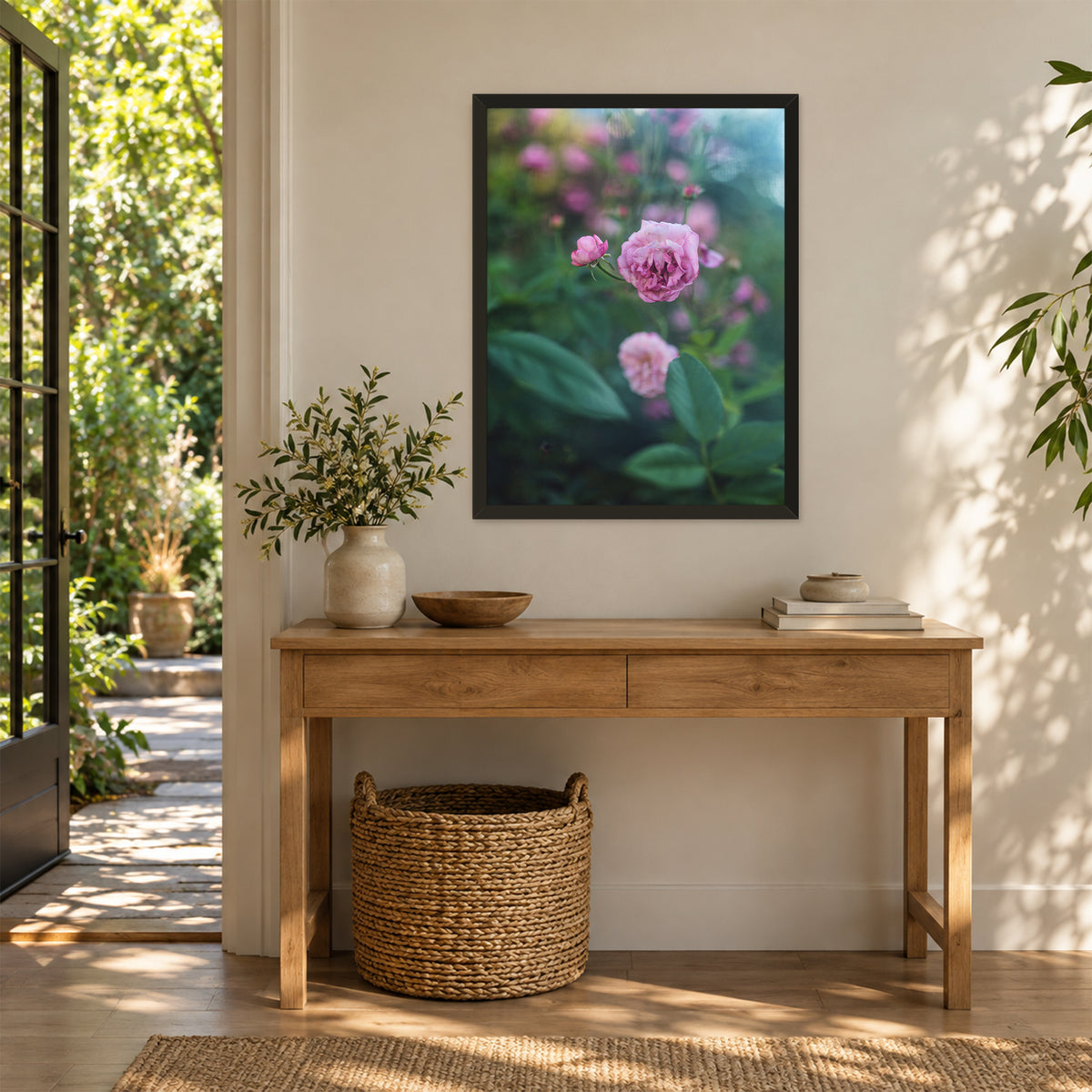 Caldwell Pink I, 18×24 inch print shown in a styled room mockup. Single pink rose rising among dark green leaves with blurred blossoms behind it. Frame shown for styling; print sold unframed.