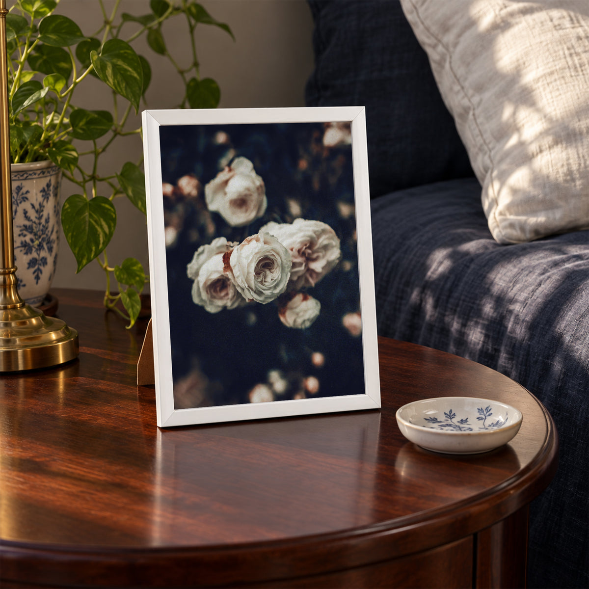 Cold Desdemona, 5×7 inch print shown in a styled room mockup. Cluster of ivory roses against a dark, softly blurred garden. Frame shown for styling; print sold unframed.