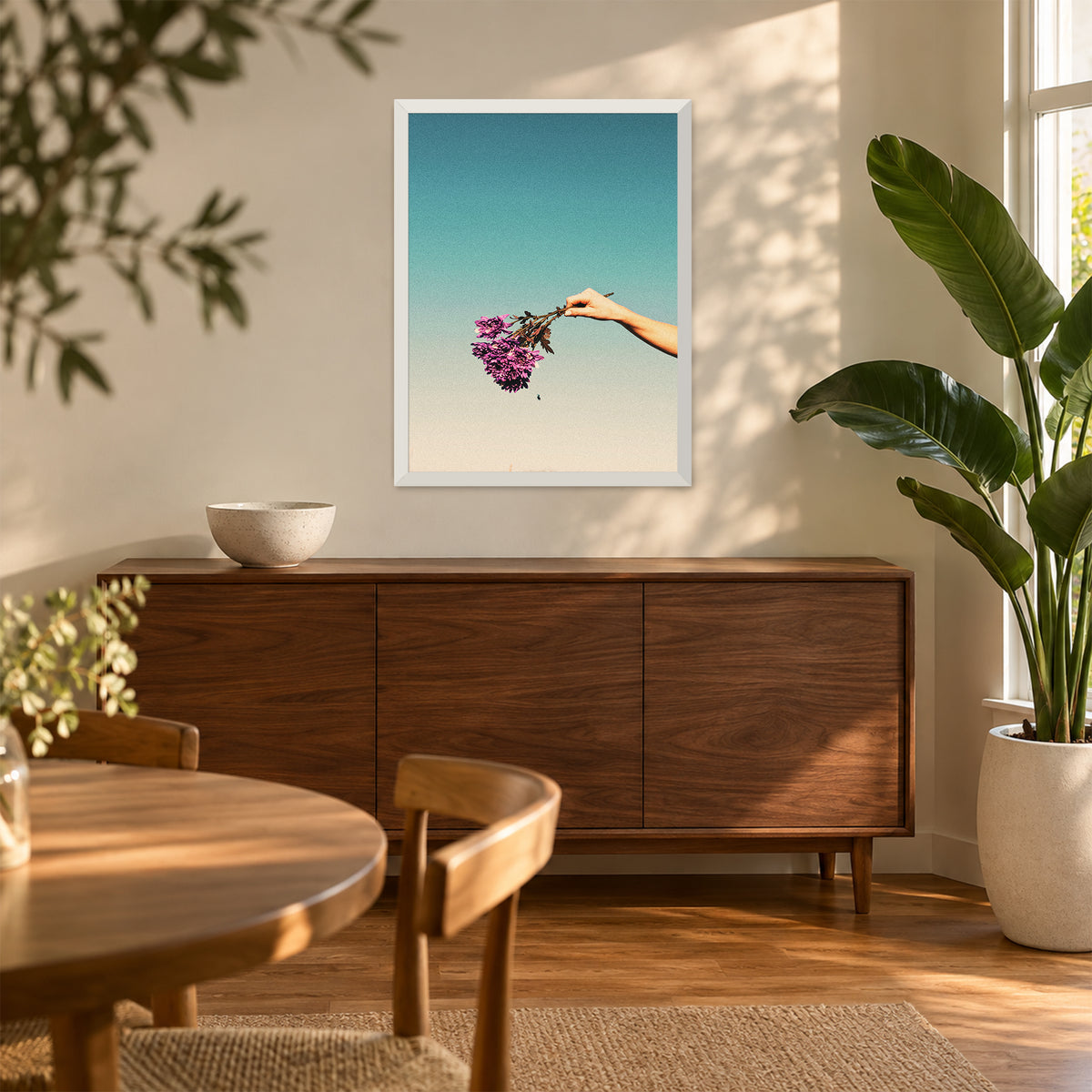 Cries of the Chrysanthemum, 18×24 inch print shown in a styled room mockup. Outstretched hand holding a small purple bouquet against a pale blue sky. Frame shown for styling; print sold unframed.