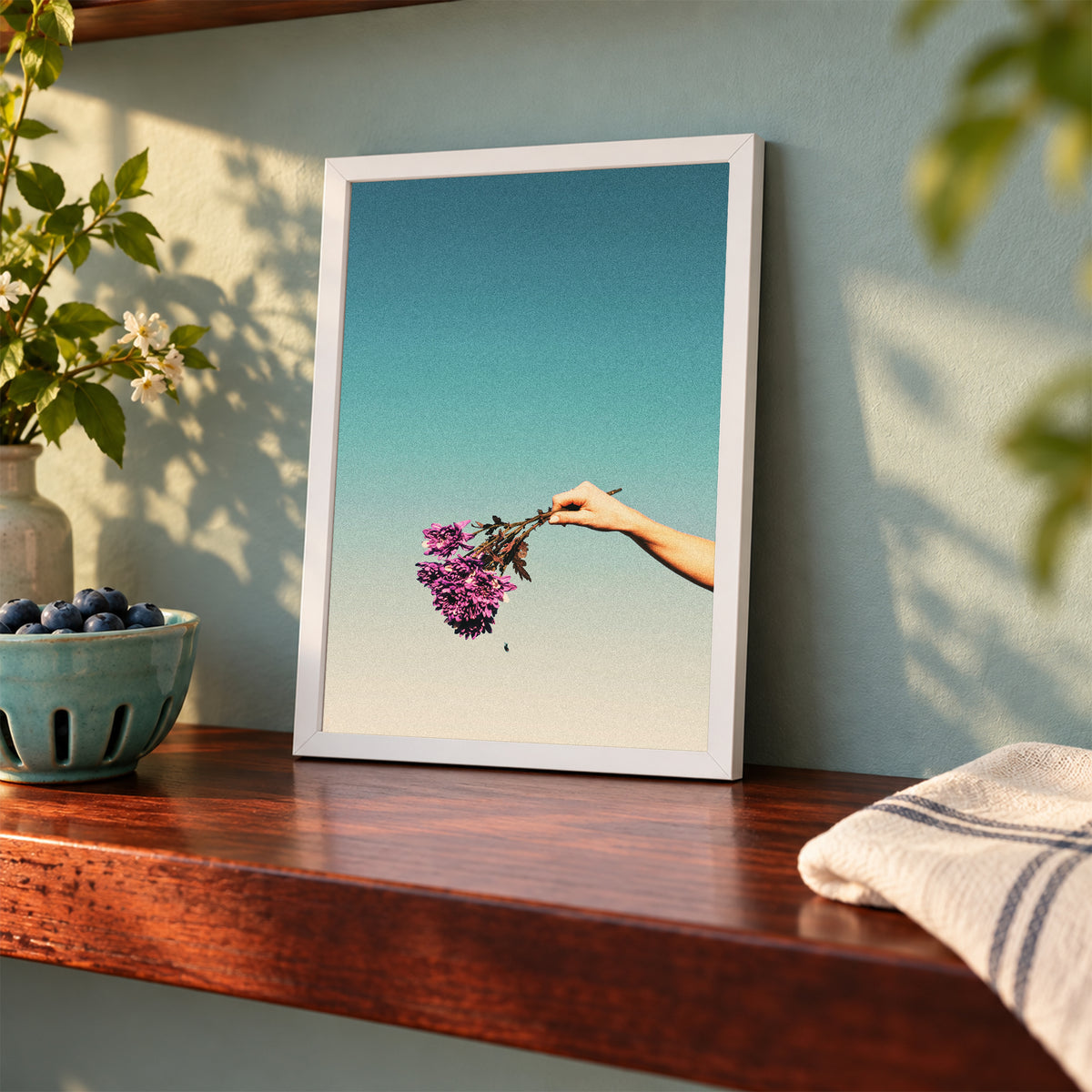Cries of the Chrysanthemum, 5×7 inch print shown in a styled room mockup. Outstretched hand holding a small purple bouquet against a pale blue sky. Frame shown for styling; print sold unframed.